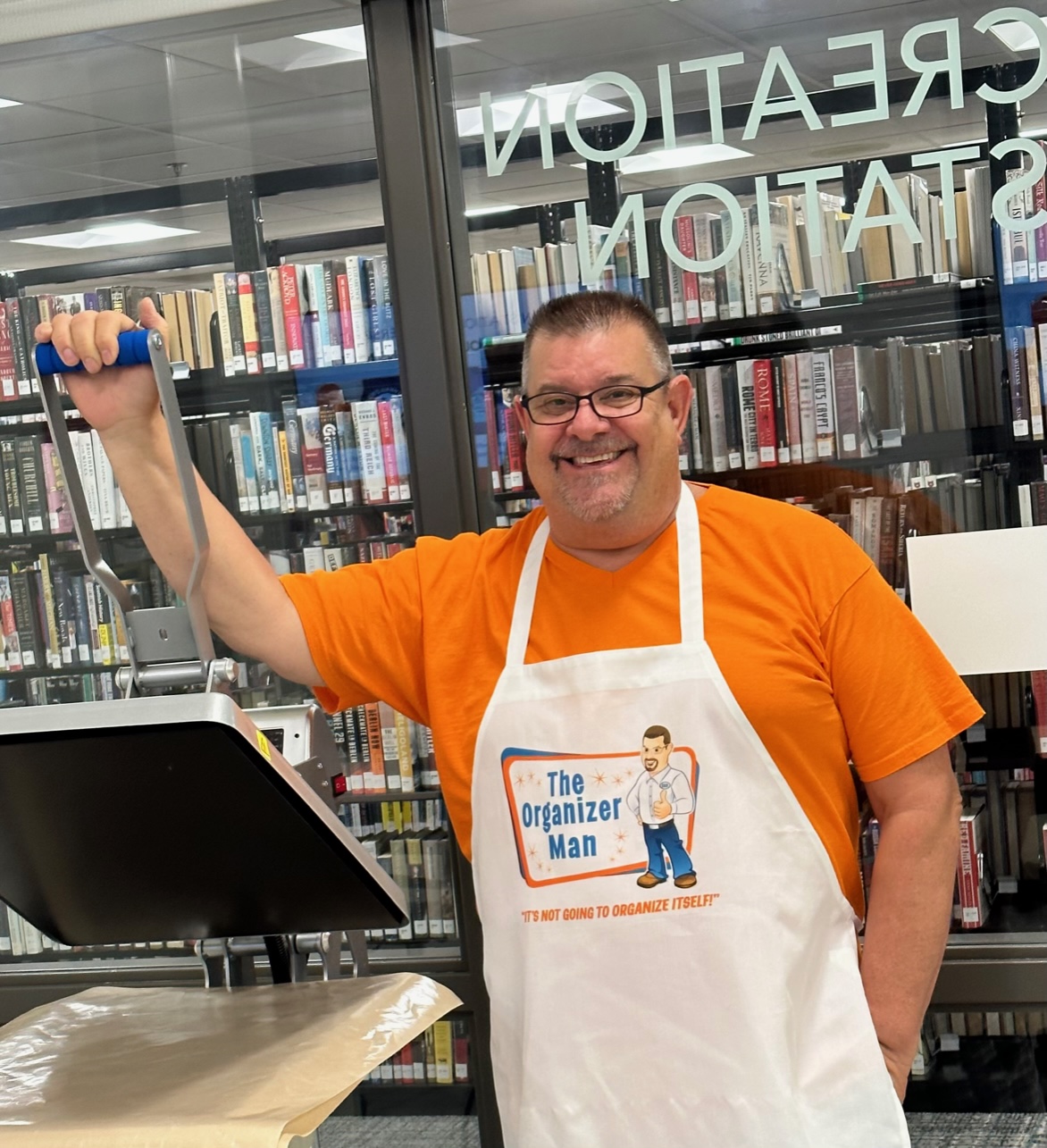 Patron wearing an apron printed with our press that reads: The Organizer Man, It's not going to organize itself!