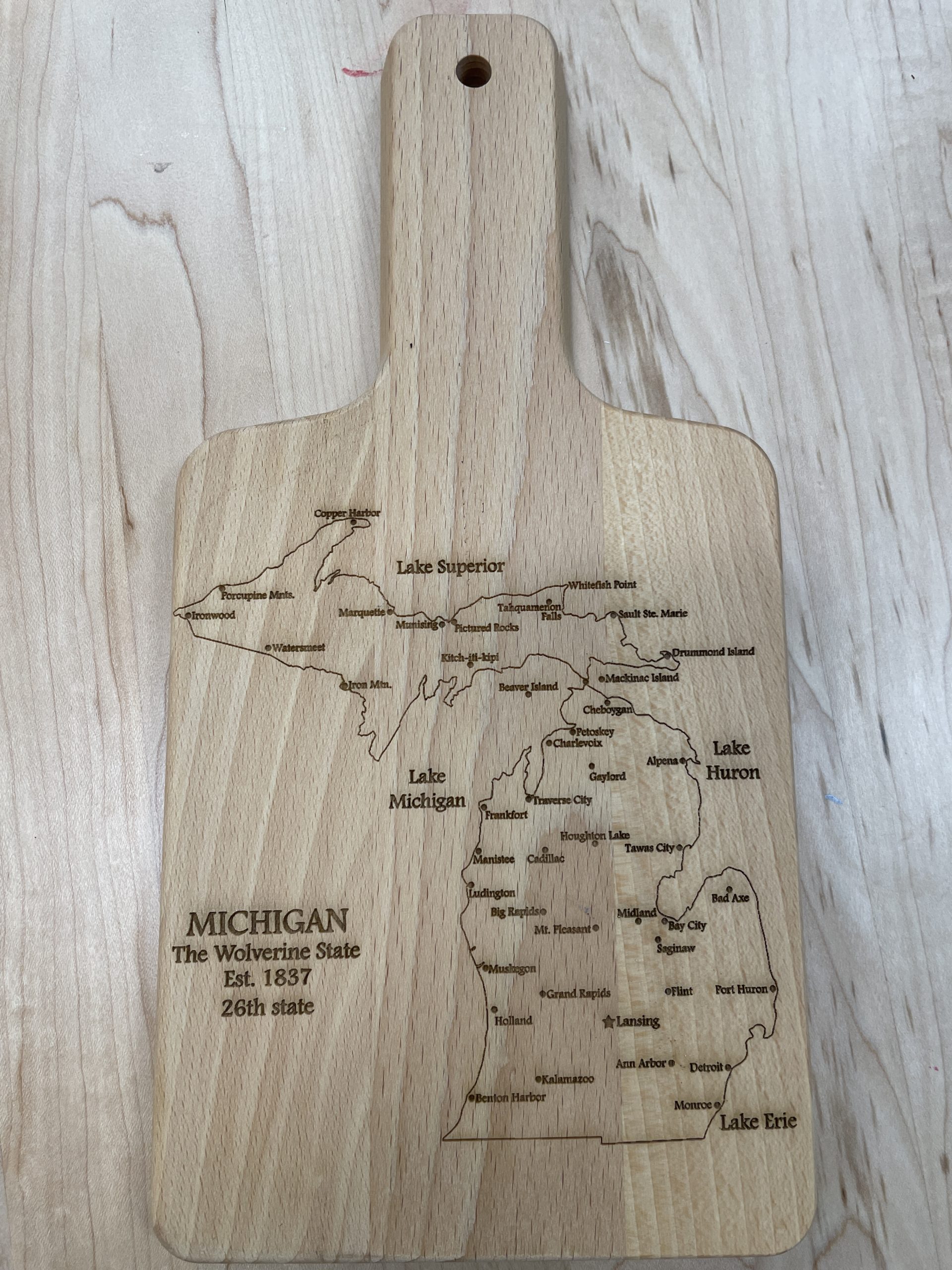 Wooden cutting board engraved with the outline of the State of Michigan labeled with major cities.