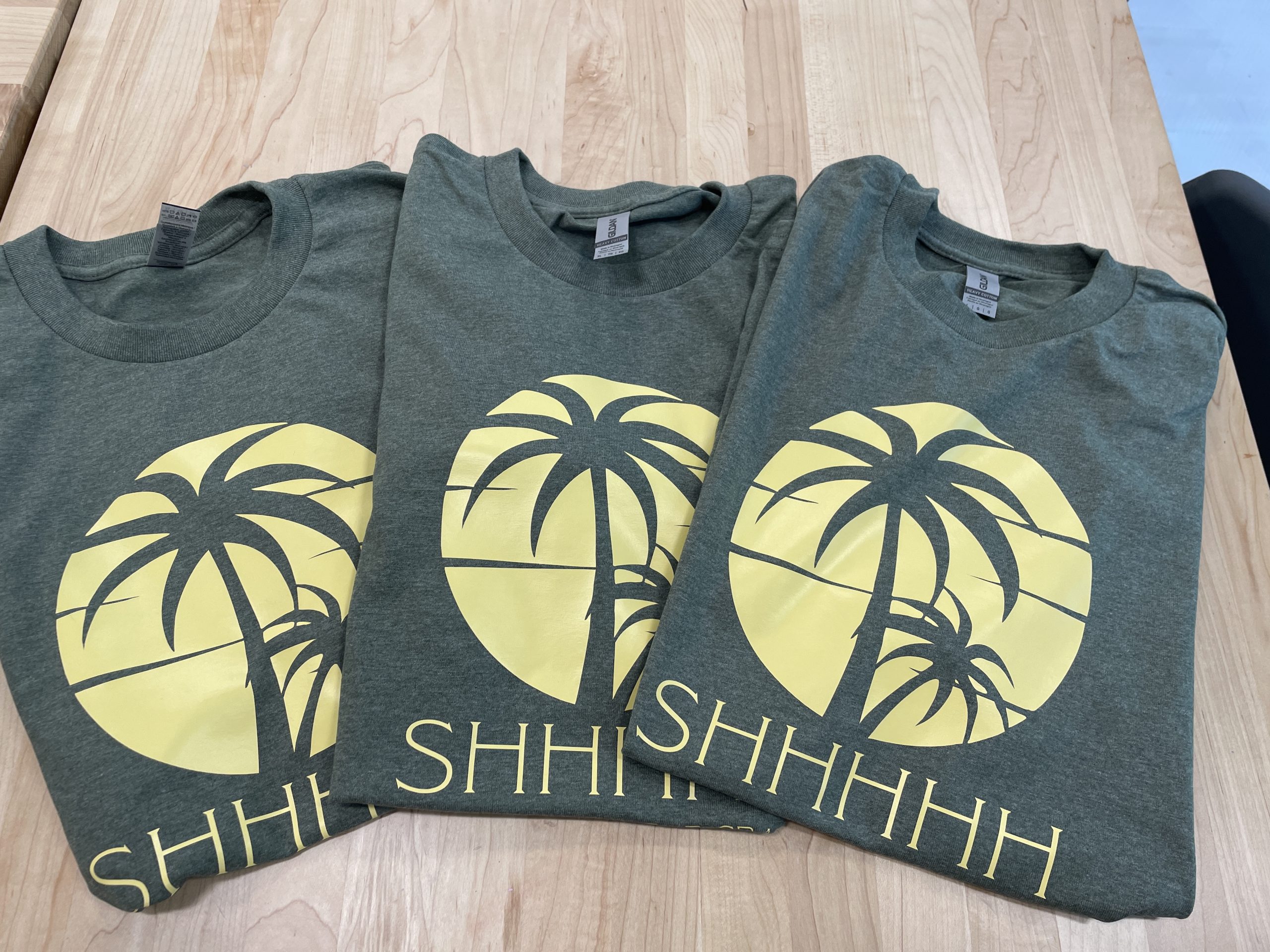 Green t-shirts printed with a yellow palm tree design.