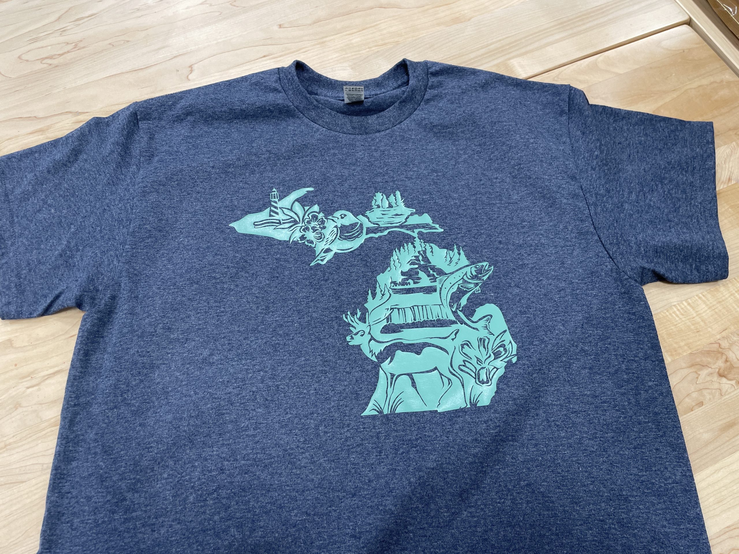Medium blue t-shirt with teal outline of the State of Michigan including hunting and fishing imagery.