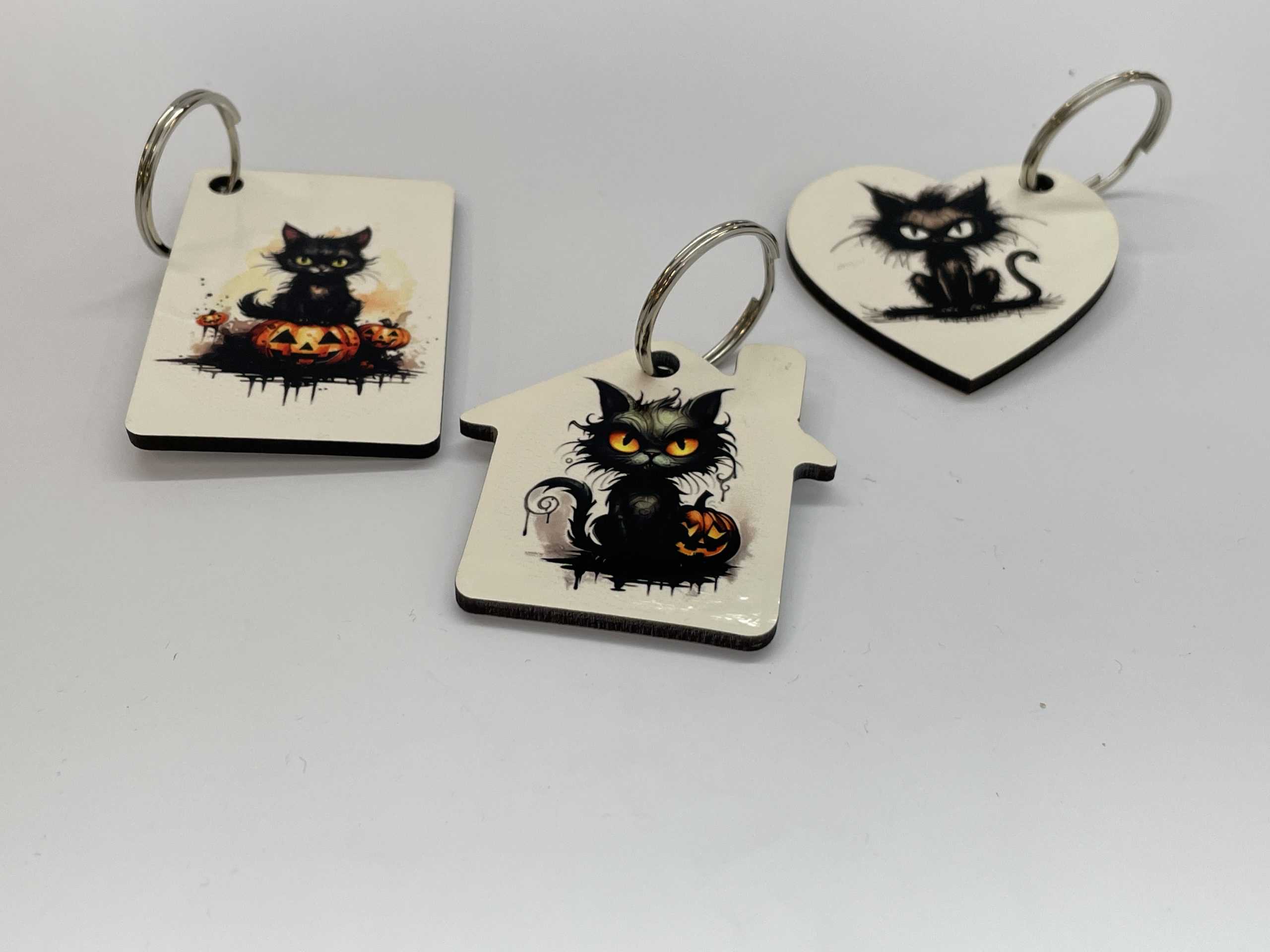 Three key chains of different shapes printed with cartoonish images of mad black cats with a Halloween motif.